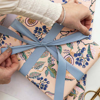 Person wrapping a gift with floral paper and a blue ribbon