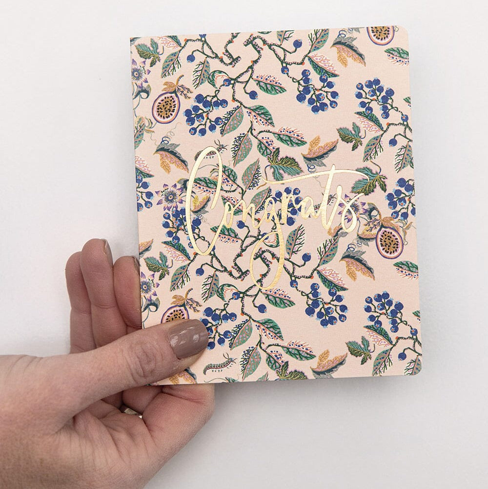 Hand holding a floral notebook with a decorative cover on a white background