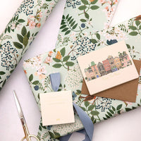 Floral-patterned gift wrap with a card, ribbon, and scissors on a white surface