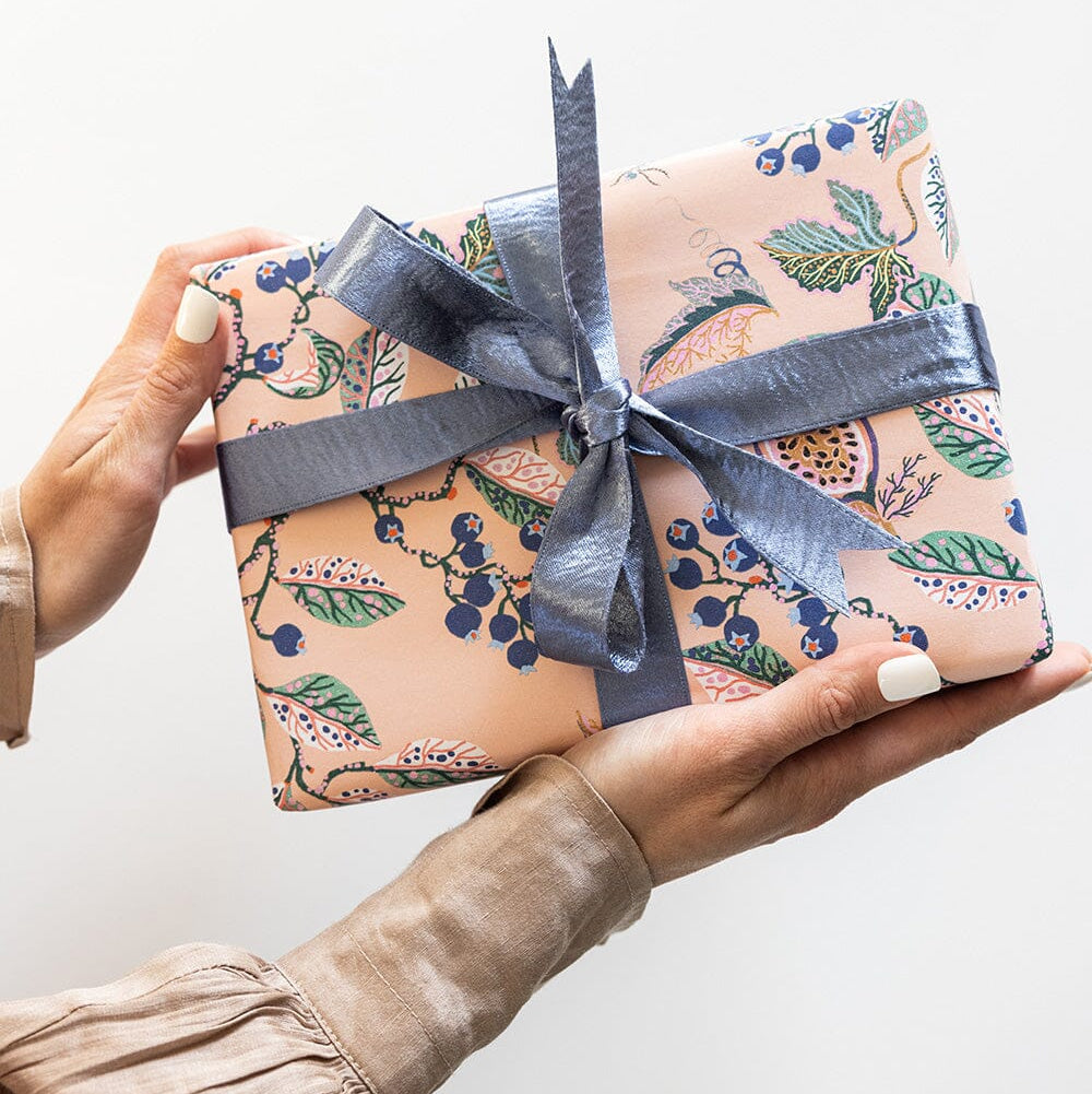 Gift box with floral pattern and blue ribbon held by a person against a white background