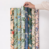 Hand holding a set of floral-patterned fabric swatches on a white background